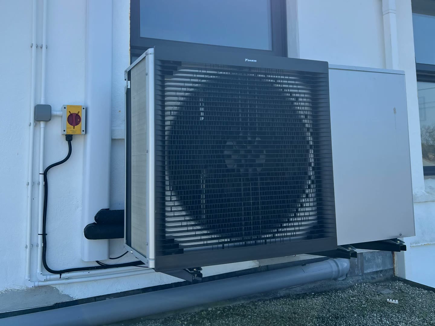 Daikin air source heat pump neatly wall-mounted on a rendered home in Newquay town, Cornwall, with tidy pipework and an isolation switch