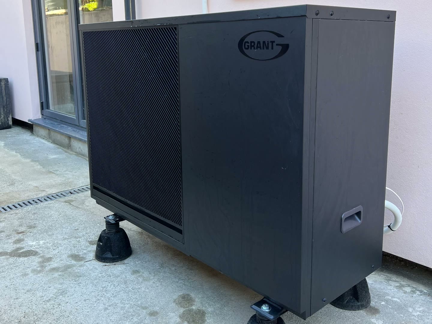 Grant air source heat pump on anti-vibration mounts outside a pink rendered home in Newquay, Cornwall, during extensive renovation and extension work